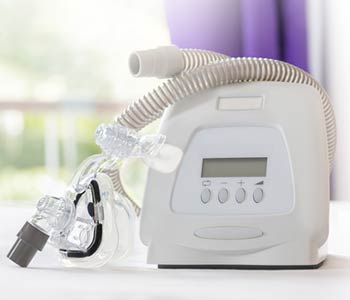 CPAP machine mask and tube on white bed cover in bedrooom blurred purple curtain background